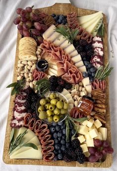 a wooden platter filled with cheeses, olives and other foods on top of a white table cloth