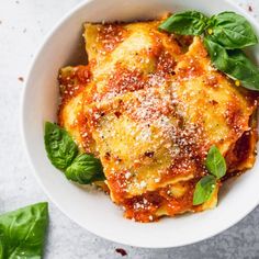 a white bowl filled with lasagna sauce and spinach leaves on top of a table