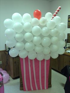 a pink cupcake with white balloons and a candy cane in the middle is on display