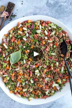 a white bowl filled with lentils, carrots and other vegetables next to two spoons