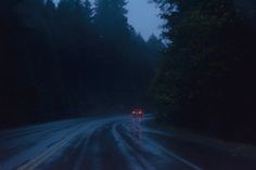 the car is driving down the road in the rain at night time, with its headlights on