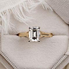 an emerald - cut diamond ring sits on top of a white furnishing blanket