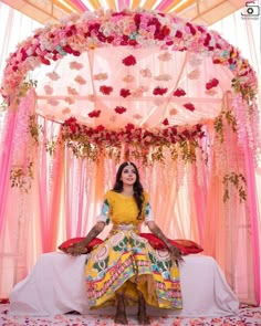 a woman sitting on top of a bed under a canopy covered in pink and yellow flowers