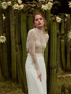 a woman standing in front of a cactus with her hands on her hips, wearing a white dress