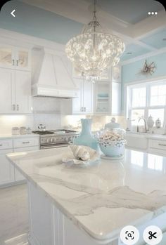 a white kitchen with marble counter tops and chandelier hanging from the center island