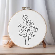 an embroidery project with flowers and butterflies in black ink on a white background, sitting on a wooden table