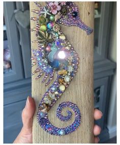 a seahorse made out of beads and other things on a piece of wood in someone's hand