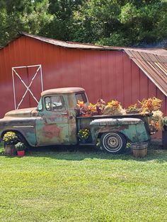 an old truck with flowers in the back parked next to a red barn and silo