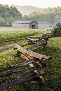 an old wooden fence with a barn in the background on a foggy, misty day