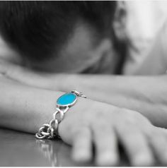 a person with their arm around a table and wearing a bracelet that has a turquoise stone on it