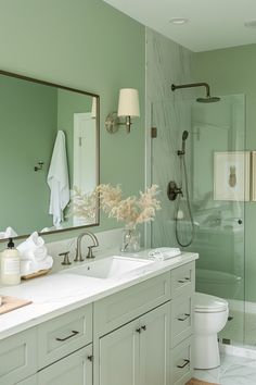 a bathroom with green walls and white counter tops, along with a large mirror on the wall