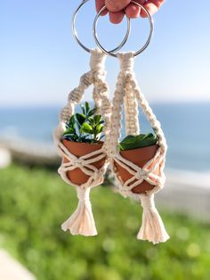 a hand holding a plant in a pot on a keychain by the beach