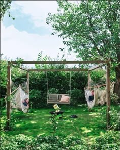 two people laying in hammocks on the grass near some trees and bushes,