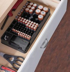 an open drawer with many batteries and tools in it next to a pair of scissors