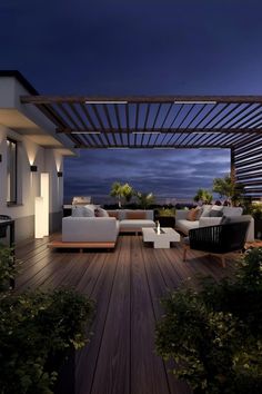 an outdoor living area with couches, tables and chairs at night on the deck