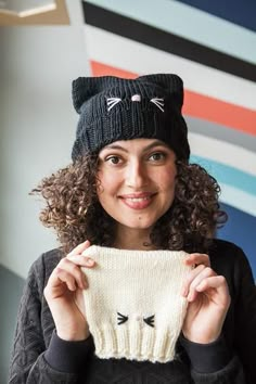 a woman holding up a knitted cat hat