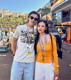 a man and woman standing next to each other in front of a race track with spectators