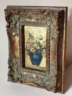 an ornate frame holds a painting of flowers in a blue vase on a white background