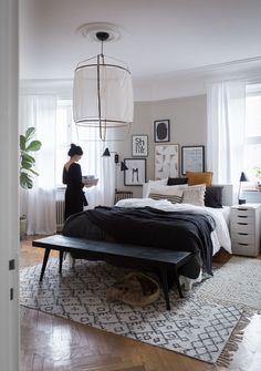 a woman standing next to a bed in a room with white walls and wooden floors