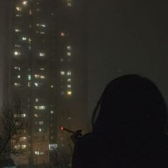 a person standing in front of a tall building at night with lights on the windows