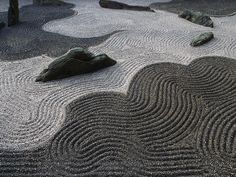 some rocks and sand in the middle of a garden with wavy lines on it's surface