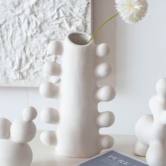 three white vases sitting on top of a table next to a book and flower