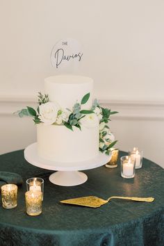 a white wedding cake sitting on top of a table next to candles and greenery