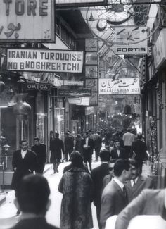 black and white photograph of people walking down the street in an old fashion town with stores on both sides