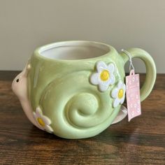 a green ceramic mug with white flowers and a tag hanging from it's handle