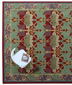 a red and green area rug with an ornament design on the border, next to a white toilet