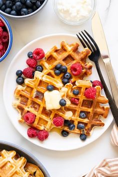 a white plate topped with waffles covered in blueberries and raspberries