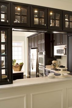 a kitchen with black cabinets and white counter tops in front of a large mirror over the sink