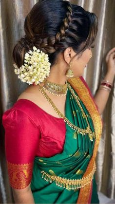 a woman wearing a green and red sari with flowers in her hair, standing next to a curtain