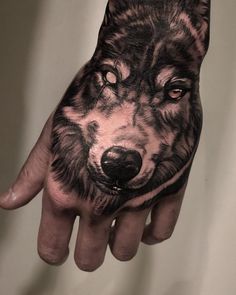 a person's hand with a wolf tattoo on it, showing the face and eyes