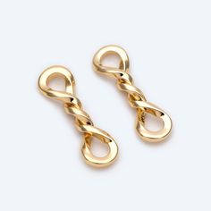 two pairs of gold colored metal earrings on a white background, one is shaped like an infinite knot