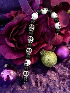 the bracelet has skulls on it and is next to a purple rose with two balls