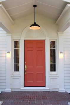 a red front door on a white house with brick walkway and light fixture above it