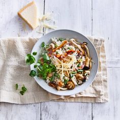 a white bowl filled with pasta and vegetables on top of a towel next to a slice of bread