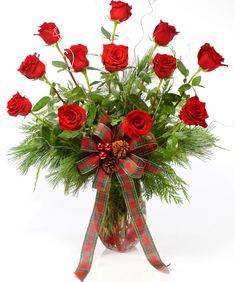 a bouquet of red roses in a glass vase with greenery and ribbon tied around it