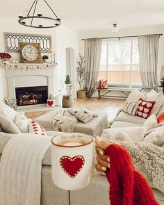 a woman holding a coffee mug in her hand while sitting on a couch with a fireplace