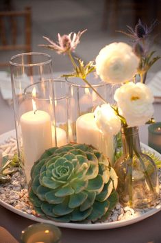 candles and flowers in vases on a plate with gravel around the edges, surrounded by rocks