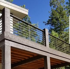 a wooden deck with metal railings next to a building and trees in the background