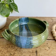 a green and blue dish sitting on top of a wooden table next to a plant