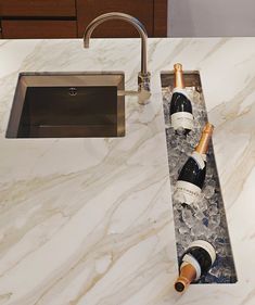 two bottles of wine sitting on top of a marble countertop next to a sink