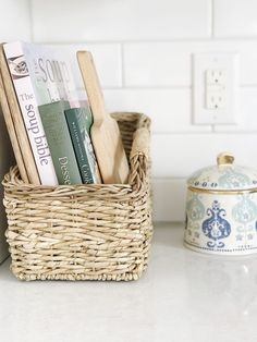 a wicker basket with books and utensils in it on a kitchen counter