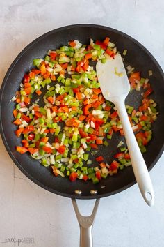 chopped vegetables being cooked in a frying pan with a spatula on the side