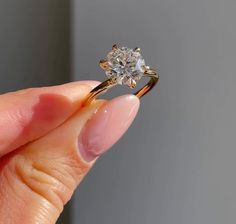 a woman's hand holding an engagement ring with a diamond in the middle, on a gray background