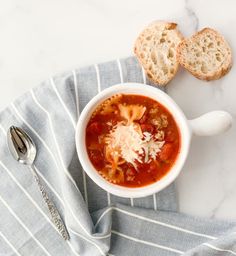 a bowl of soup with meat and cheese in it next to two slices of bread