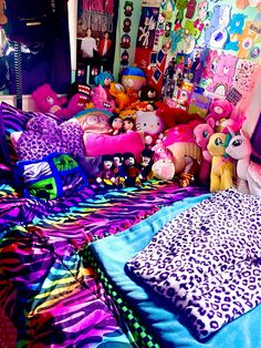 a room filled with lots of stuffed animals on top of colorful blankets and pillows,