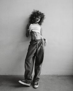 a black and white photo of a woman leaning against a wall with her hands on her hips